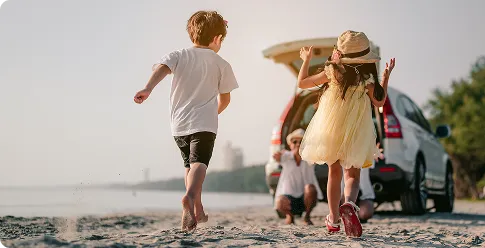 Niños corriendo por la playa felices y madre traquila con su seguro Sanitas